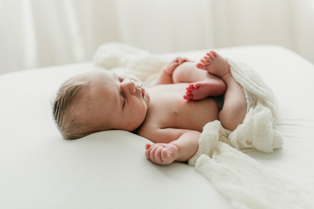 newborn photographer documents snuggly baby laying on an all white natural setting for lifestyle images