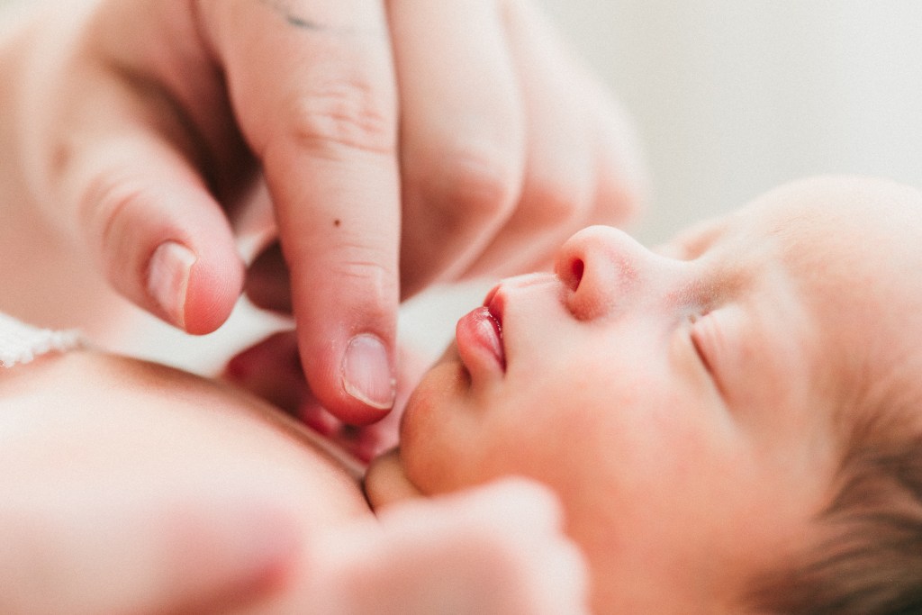 Naturally posed newborn image of a baby laying on her back and close up detail photo of her lips with her moms hand near photographed by Heidi Rakas Photography in Eugene, Oregon
