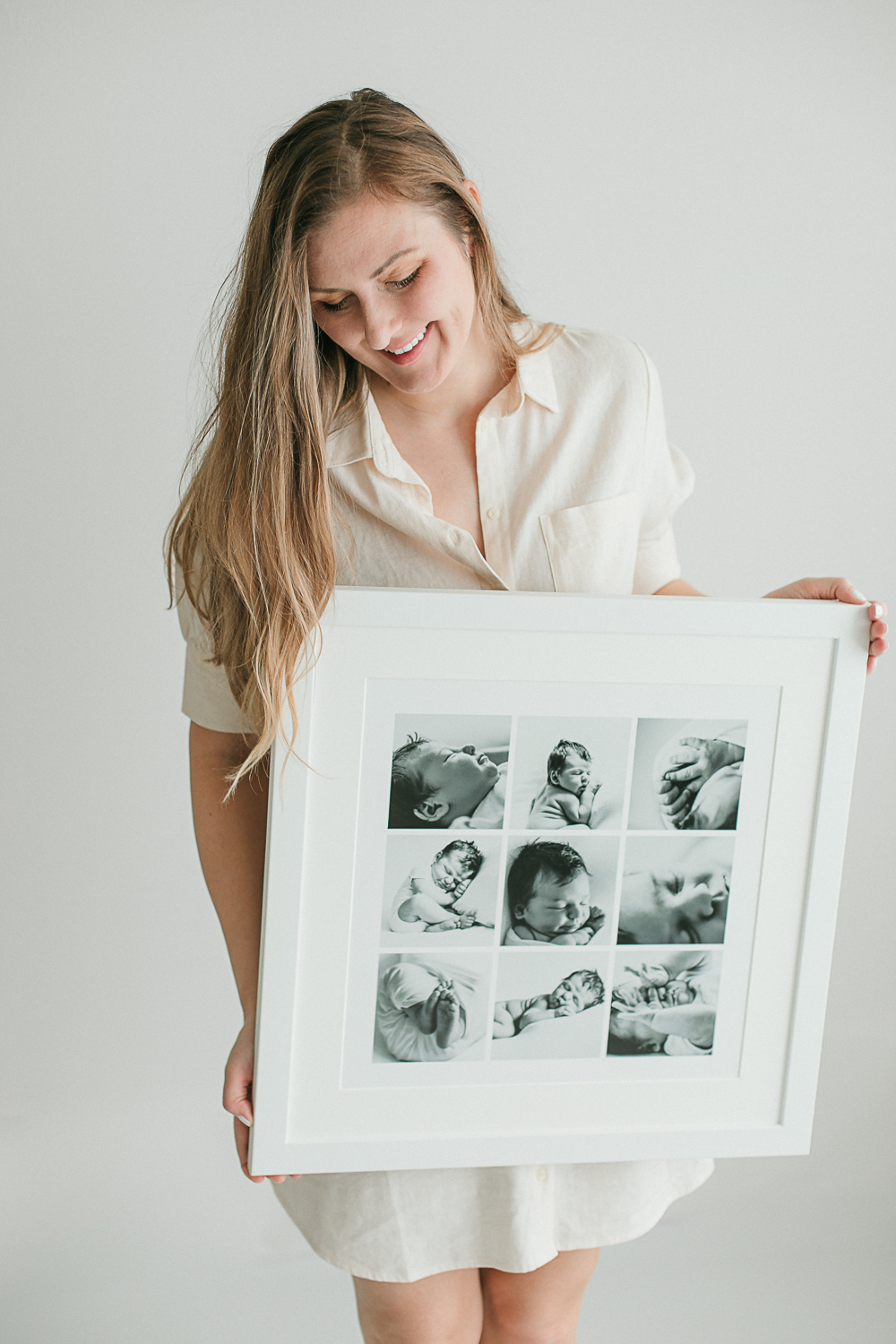 Eugene photographer Heidi Rakas holding a beautiful framed piece of artwork featuring a newborn photos in her eugene photo studio