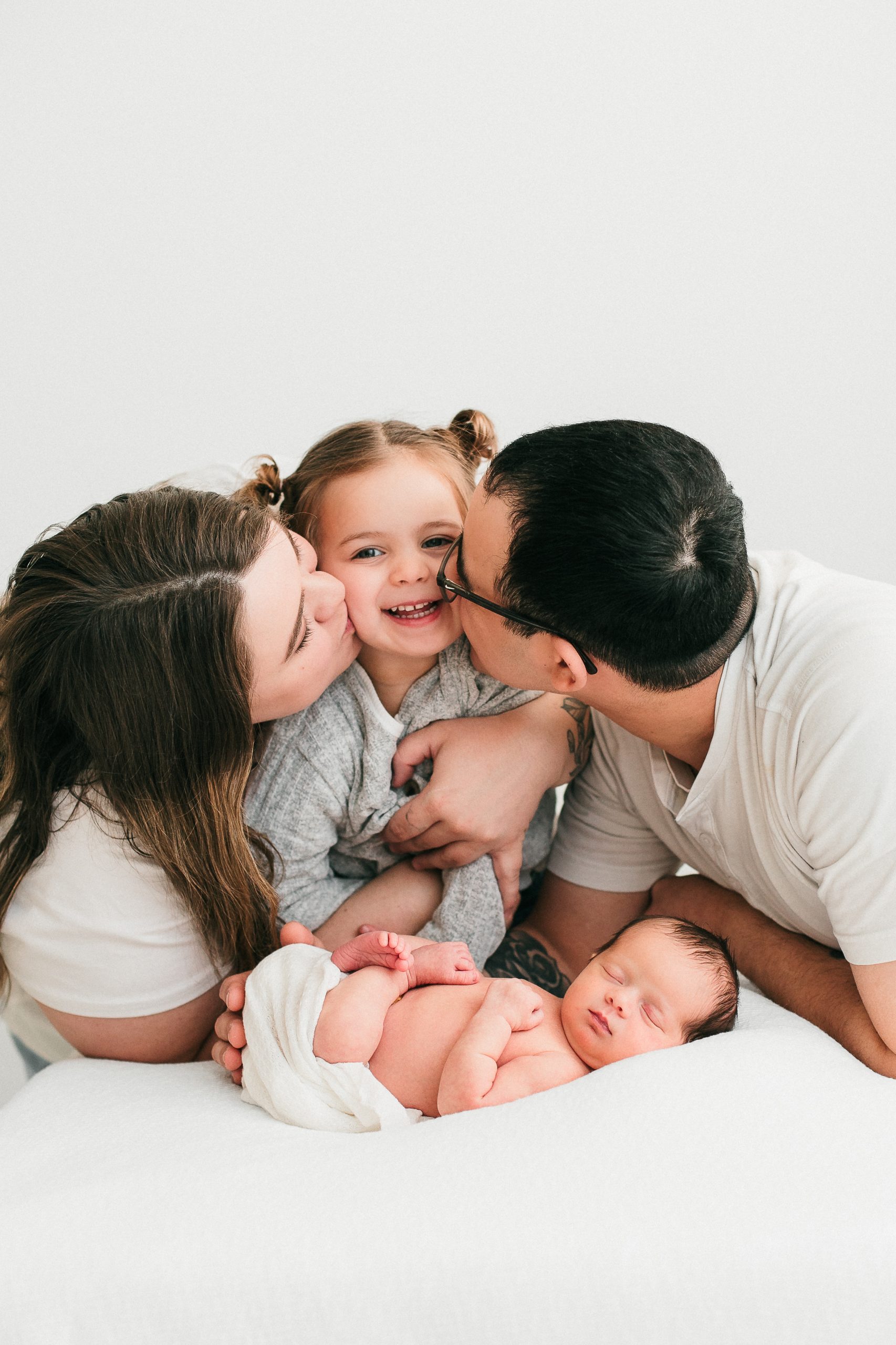 toddler with her family being kissed on the cheek by her parents during newborn phtooshoot