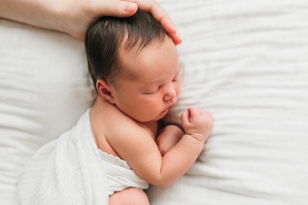 a newborn baby boy laying down with his mom gently touching his head during his newborn session in eugene oregon for Heidi Rakas Photography
