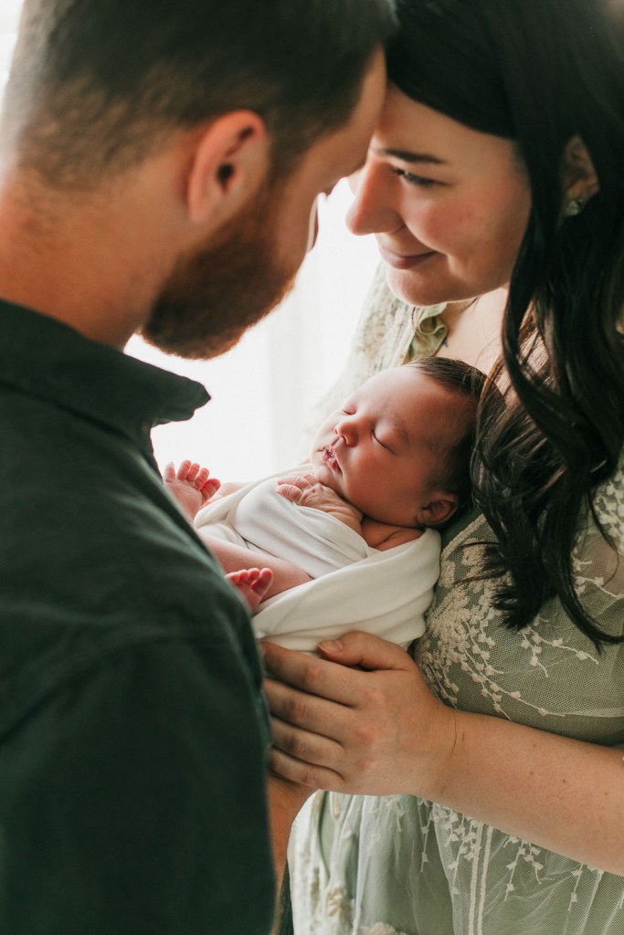 a mom and dad holding their newborn baby during their newborn session in eugene oregon with so much love and emotion in their eyes